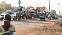 Eine gepanzerte Kfz-Patrouille fährt durch die Stadt. Rechts fahren Tuk-Tuks vorbei, im Vordergrund stehen zwei Kinder