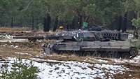 Auf schneebedeckter Heide steht am Waldrand ein Panzer mit einer gesetzten kleinen, grünen Flagge.