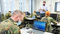 Ein Klassenraum mit Soldaten. Sie sitzen an Computern und tragen alle eine Maske