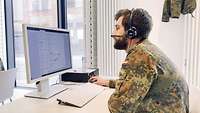 Ein Soldat hat ein Headset#en auf seinem Kopf und sitzt vor einem Monitor.