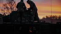 Bei Sonnenaufgang stehen zwei Soldaten am Turm eines Schützenpanzers Puma.