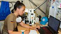 Eine Soldatin sitzt vor ihrem Laptop und schaut sich Aufnahmen aus dem Mikroskop an
