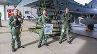 Drei Soldaten stehen vor einem Eurofighter. Einer von ihnen hält eine Erinnerungsurkunde in der Hand.