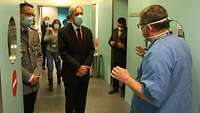 Ein Mann in einem Anzug steht in einem Gang und lässt sich von einem Arzt in Krankenhauskleidung etwas erklären