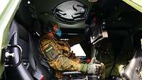 Ein Soldat sitzt in einem Fahrzeug und hält in seiner Hand einen Joysticks fest und schaut dabei auf einen Monitor. 
