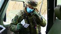 Ein Soldat steht an einer geöffneter Fahrzeugtür und hält den Hörer eines Funkgerätes in der Hand.