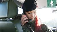 Eine Soldatin sitzt in einem Geländefahrzeug und hat einen Funkgerät-hörer in der Hand