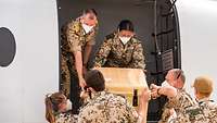 Eine Soldatin und ein Soldat heben eine Transportbox aus einem Flugzeug. Vier weitere Soldaten nehmen die Kiste entgegen