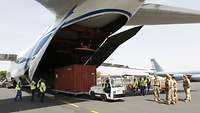 Eine großes Flugzeug mit geöffneter Ladeklappe steht auf einem Flugplatz. Ein Container wird gerade entladen.