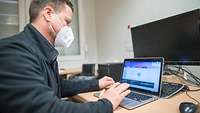 Ein Mann mit Mund- und Nasenschutzmaske arbeitet an einem Laptop