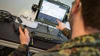 Ein Soldat zeigt mit seiner rechten Hand auf den Monitor des Systems.