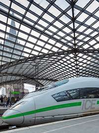 ICE in neuem Design mit grünem Streifen am Kölner Hauptbahnhof unter der Glaskuppel, im Hintergrund der Kölner Dom.