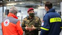 Ein Mann in Uniform spricht mit zwei Mitarbeitern ziviler Rettungsorganisationen.