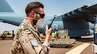 Ein Soldat steht mit einem Funkgerät vor einem Transportflugzeug