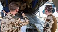 Zwei Soldaten stehen an der geöffneten Ladeluke eines Transportflugzeuges und besprechen die Entladung eines Transportpanzers