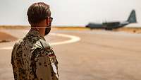 Ein Soldat steht auf dem Flugfeld und schaut zu einem Flugzeug, das im Hintergrund gerade gelandet ist