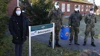 Eine Zivilistin und drei Soldaten stehen im Freien vor einem flachen Gebäude aus roten Klinkersteinen.