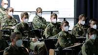 Zehn Soldaten und Soldatinnen sitzen mit Mund-Nasenbedeckung in einem Hörsaal.