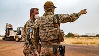 Zwei Soldaten stehen vor zwei Baumaschinen. Ein Soldat zeigt mit der Hand nach rechts