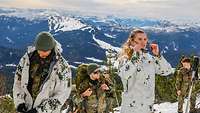 Vor dem Hintergrund eines Bergpanoramas ziehen Soldaten die Schneetarnanzüge über ihre Uniform an.