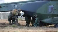 Vier Soldaten steigen hinten über die Rampe in einen Hubschrauber ein, der auf einem Feld steht.