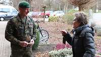 Ein freundlich blickender Soldat in Flecktarnuniform und eine ältere Dame unterhalten sich im Freien.