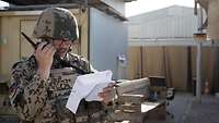 Ein Soldat mit Weste und Helm hält sich das Handfunkgerät vor das Gesicht, in der Hand hält er einen Zettel 