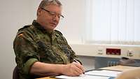 A soldier sitting at a desk signs a sheet of paper