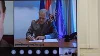 The monitor shows a soldier signing a sheet of paper