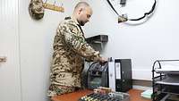 Ein Soldat steht in einem Büro und zählt mittels einer Geldzählmaschine Bargeld