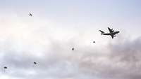 Am Himmel fliegt ein Flugzeug aus dem Fallschirmspringer springen. Im Hintergrund ein weiteres Flugzeug