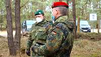 Zwei Soldaten mit Mund-Nasenbedeckung stehen in einem Wald und unterhalten sich.