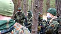 Mehrere Soldaten stehen im Wald und sprechen miteinander.