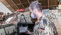 Ein Soldat steht neben einem Spähwagen Fennek und liest die Fahrzeugdaten an einem Bildschirm aus