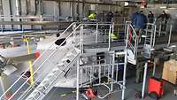 Ein Hubschrauber Sea Lion steht im Hangar des EGV zwischen einem Arbeitsgerüst, auf dem sich mehrere Personen befinden.