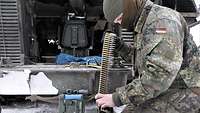 Ein Soldat kniet vor der Heckklappe seines Schützenpanzers. Er bereitet einen Munitionsgurt für das Maschinengewehr vor