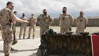 Ein deutscher Soldat erklärt einem weiteren die auf einem Tisch liegenden Waffen. Zwei belgische Soldaten schauen zu