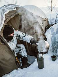 Ein Soldat sitzt im Schnee im Eingang seines Zelts und bereitet heißes Wasser vor