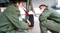Major Iwersen und Gabriel sind unter einem Eurofighter in die Hocke gegangen und sprechen miteinander