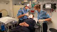 Ein Soldat liegt auf einem Zahnarztstuhl und wird von einem Zahnarzt und einer Zahnarzthelferin untersucht 