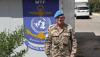 Ein Soldat mit blauem Barett steht vor einem Gebäude, an dem ein Schild mit der Aufschrift UNIFIL MTF hängt