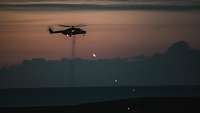 In the evening twilight, tracer ammunition is discharged from a helicopter hovering in the air.