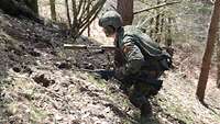 Ein Soldat mit zwei Waffen in den Händen läuft im Wald einen Berg hoch.