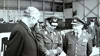 Ein Mann in Zivil und zwei Männer in Bundeswehruniform. Der Mann in der Mitte legt 