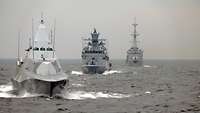Three grey warships in a line at sea.