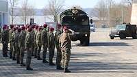 Zahlreiche Soldaten mit rotem Barett sind angetreten. Ein Lkw, von dem aus eine Soldatin militärisch grüßt, fährt vorbei.