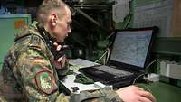 Ein Soldat sitzt in einer Kabine an einem Computer.