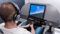 Ein Mann sitzt vor einem Monitor und steuert mit einem Joystick ein Flugzeug.