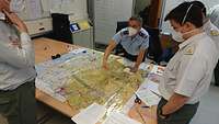Oberstleutnant Dirk Heinzmann zeigt auf eine Karte, die vor ihm auf dem Tisch liegt. Lehrgangsteilnehmer hören zu