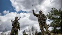 Zwei Soldaten stehen auf einer Wiese und lassen den roten Wetterballon mit einer kleinen Sonde unter dem Ballon steigen.